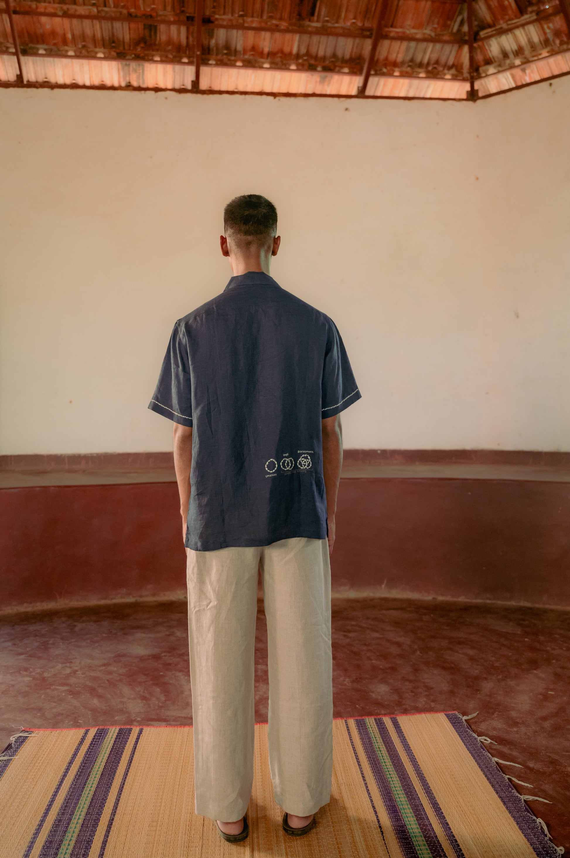 man in a blue linen shirt hand-embroidered with different loops standing in a yoga hall. Half sleeve shirt, Material: linen, Back view