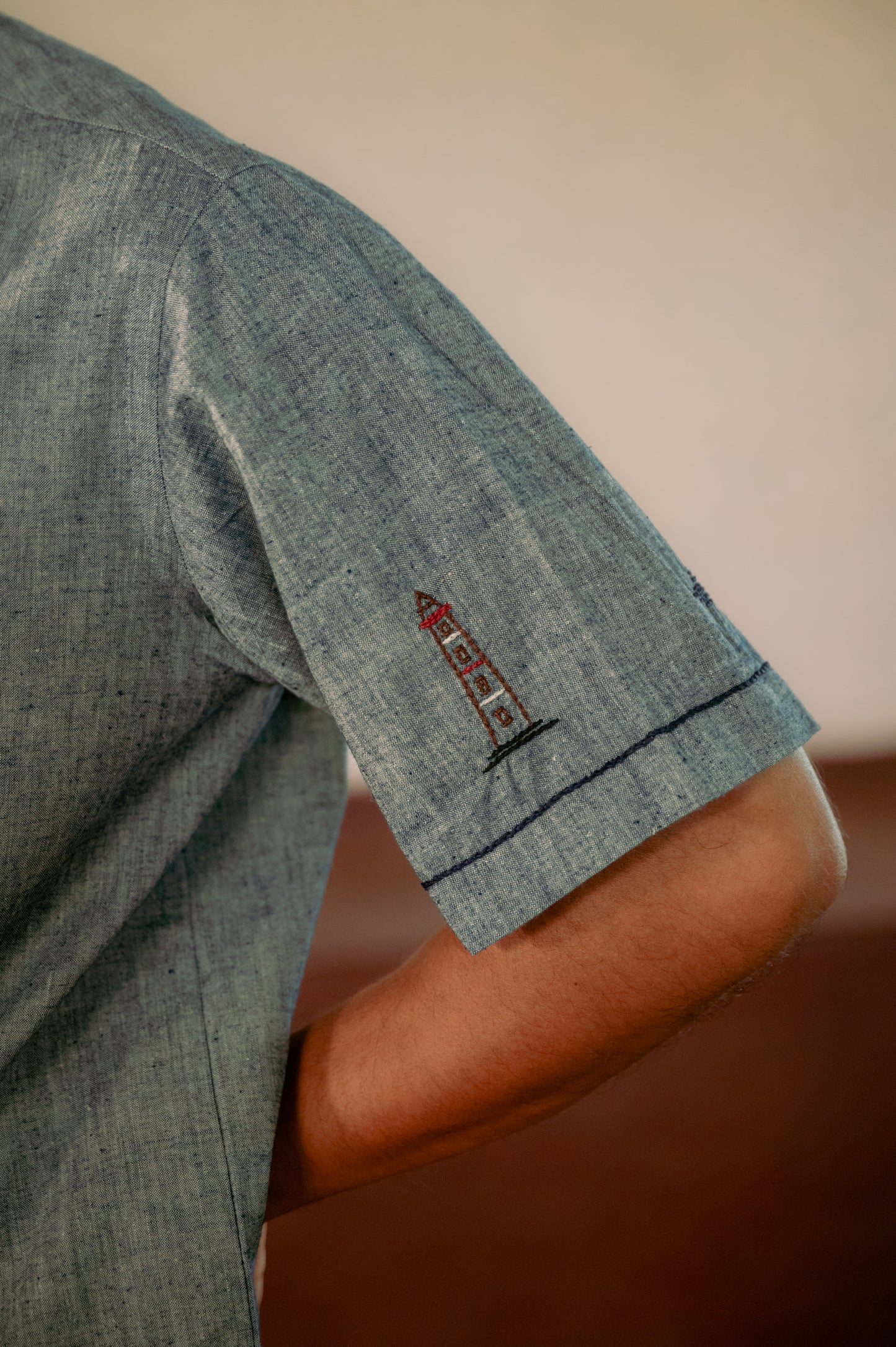 left hand sleeve detail of an organic blue shirt- a lighthouse and a boat are embroidered on the sleeve