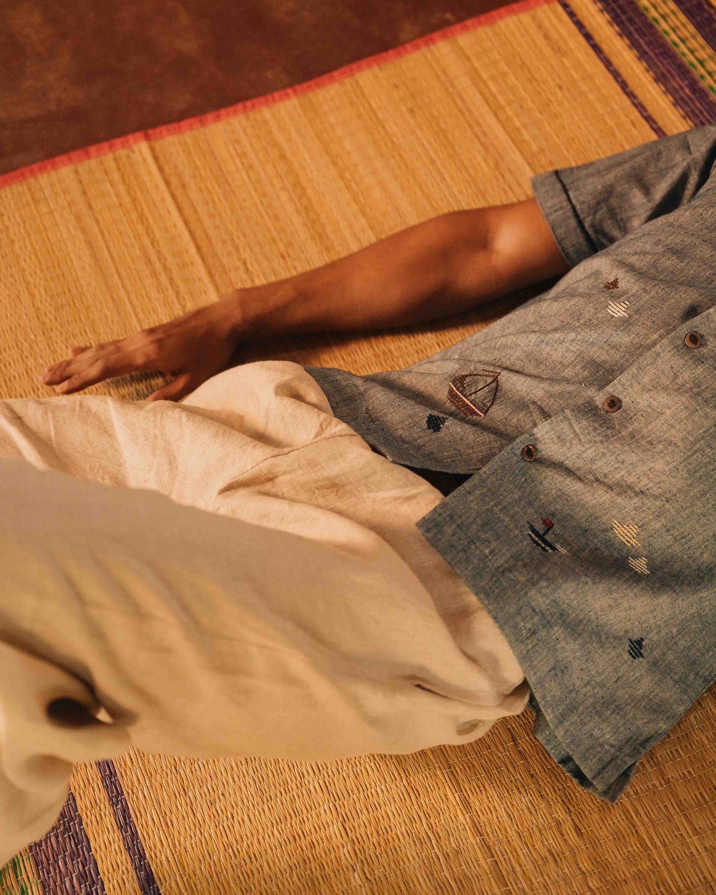 a man laying down on a bamboo mat wearing beige linen lounge pants