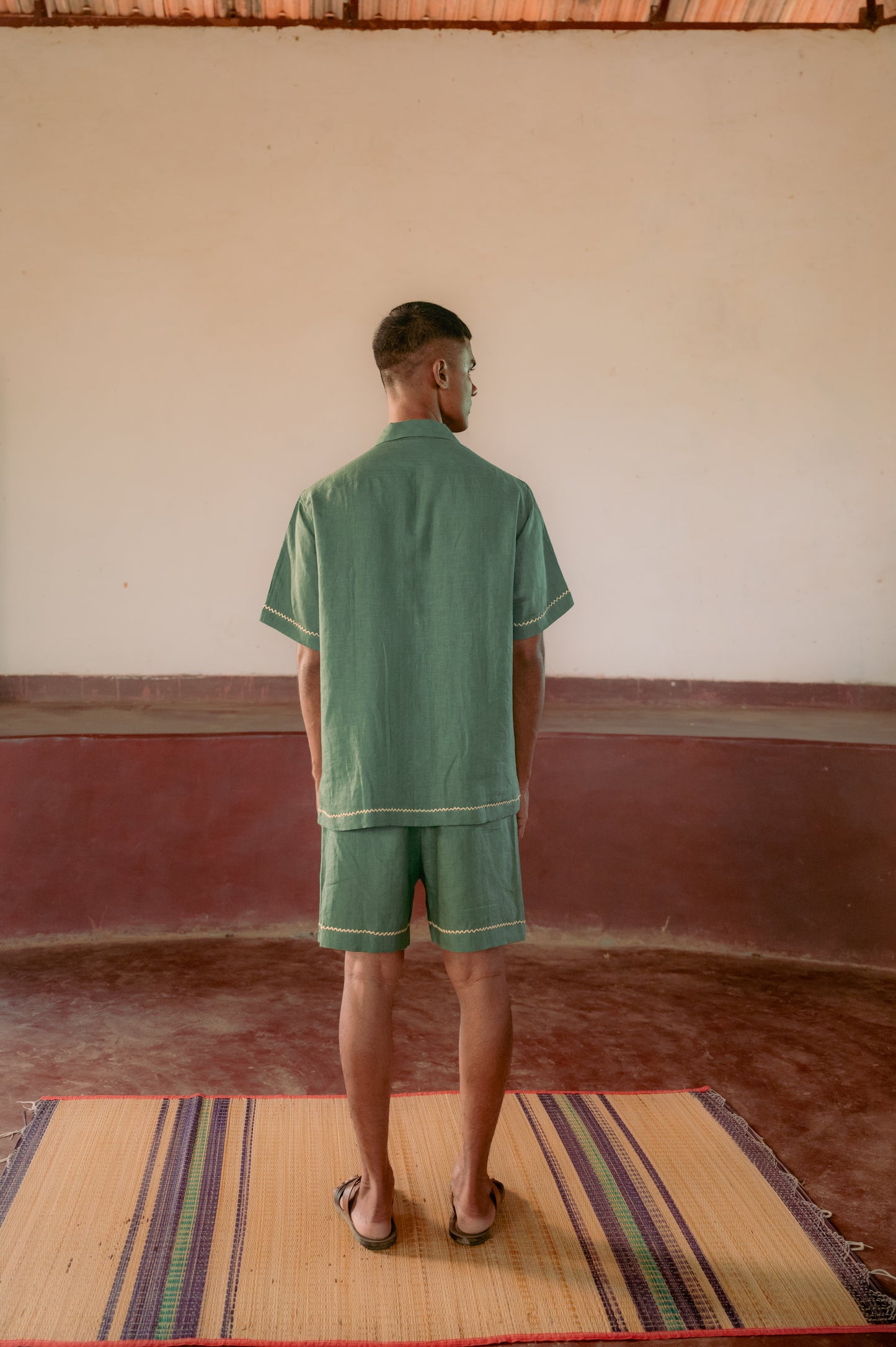 back view of a man in a green hand-embroidered  linen shirt standing in a yoga hall. Half sleeve shirt, Material: linen, Back view