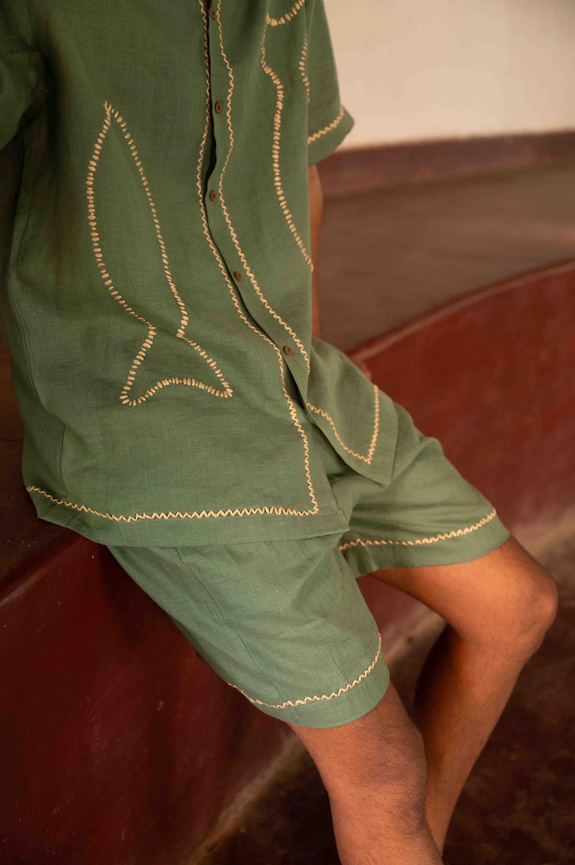 a man sitting in a yoga hall in green linen hand embroidered edges and fishes