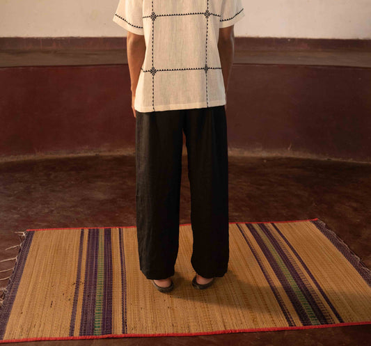 A man standing in a yoga hall wearing black linen lounge pants. Back view