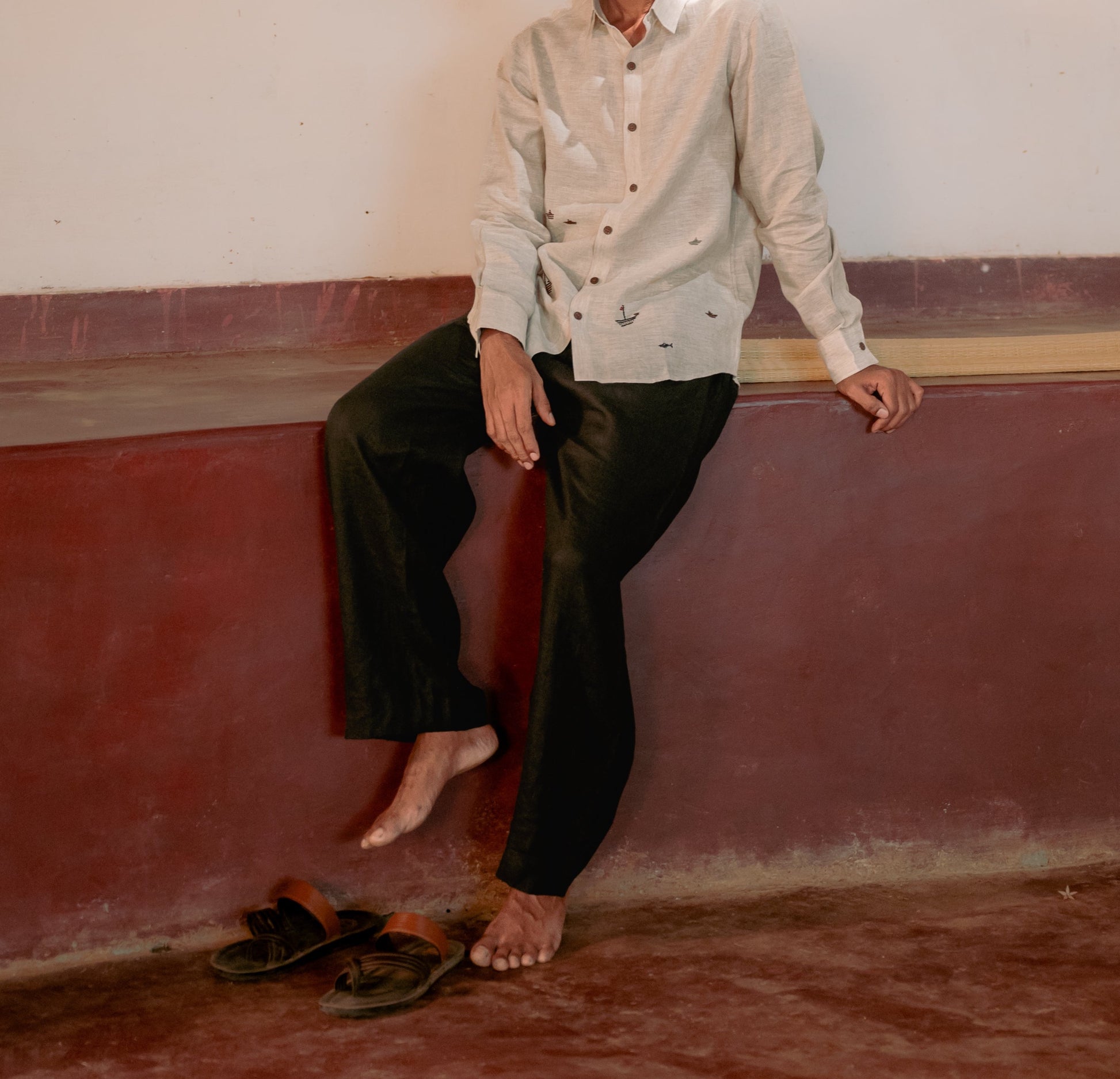 A man sitting in a yoga hall wearing black linen lounge pants.