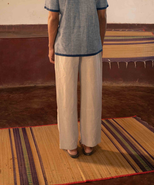 A man standing in a yoga hall wearing dark beige linen lounge pants. Back view