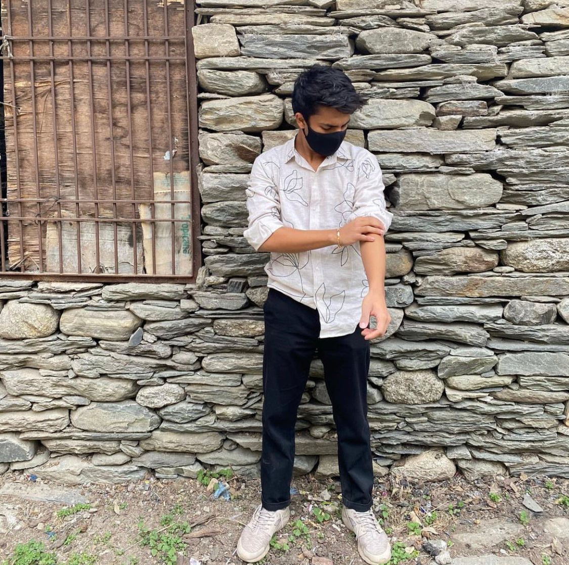 Pranav in a full sleeved beige linen shirt is standing in front of a stone hut