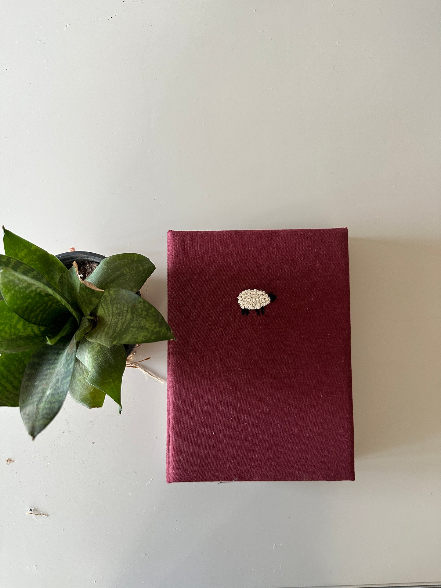 A maroon cover diary made with maroon linen scraps with a white sheep embroidered on the cover