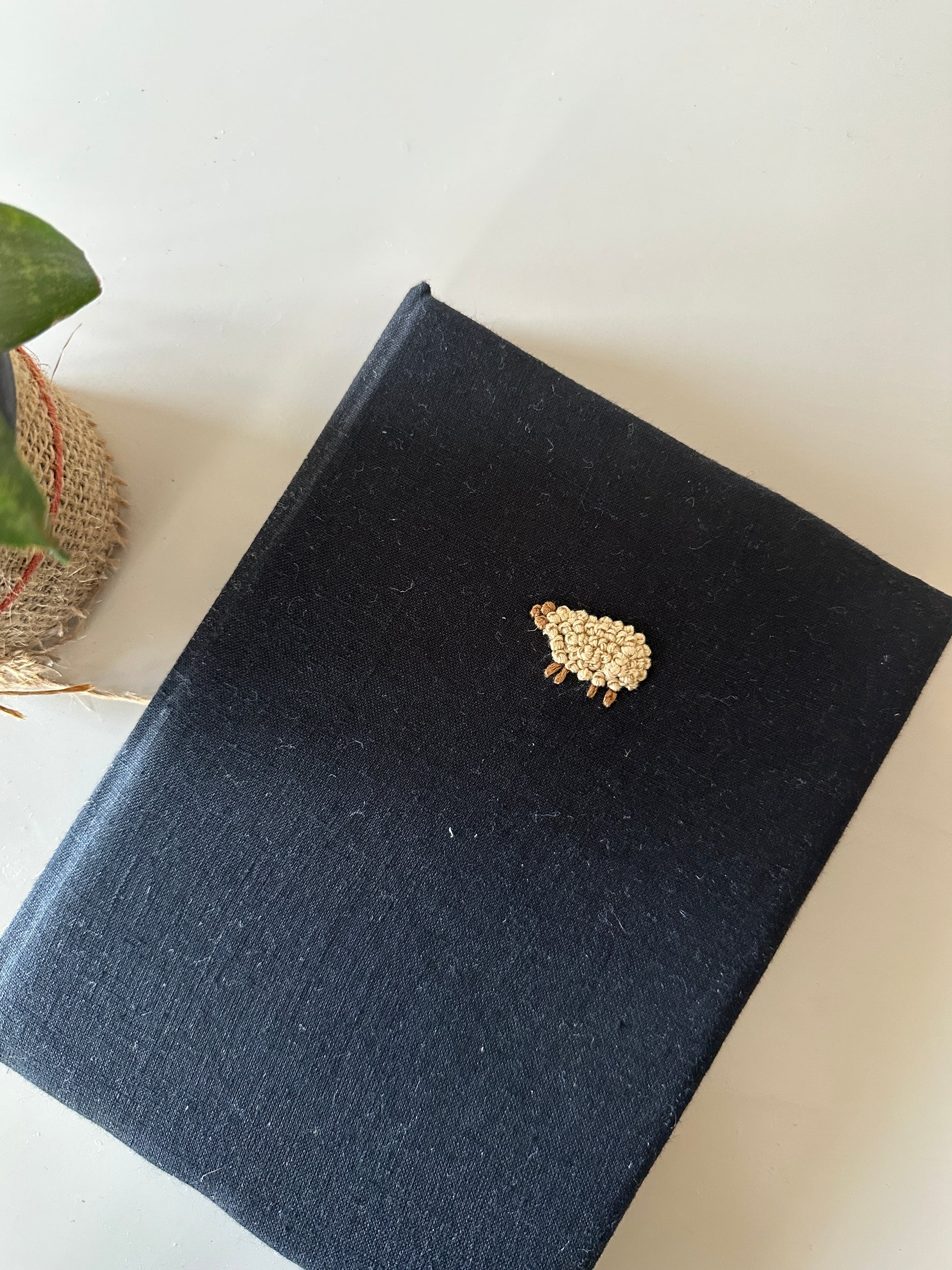 A black cover diary made with black linen scraps with a beige sheep embroidered on the cover