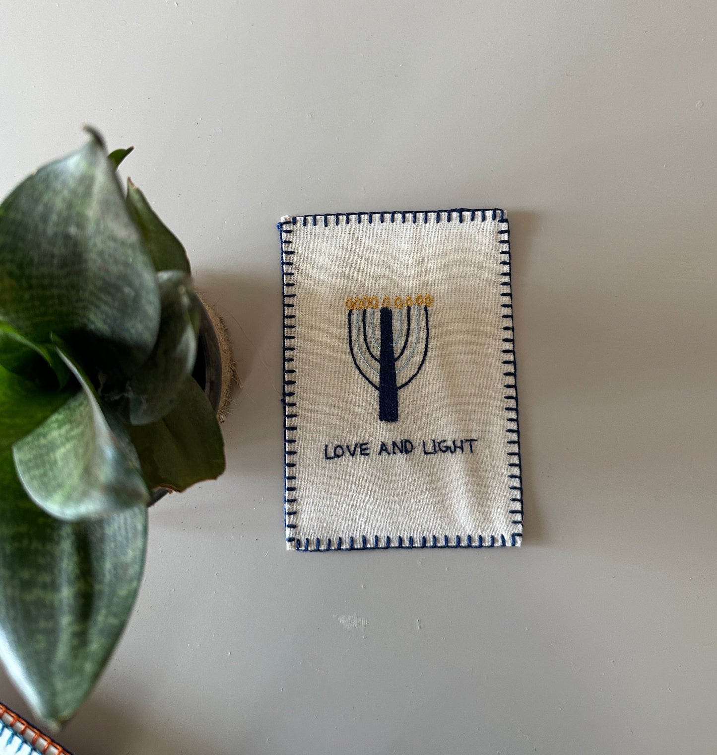 Hand-embroidered postcard with a Hanukkah candle stand and the words 'Love and Light,' crafted from sustainable linen, ideal for holiday greetings