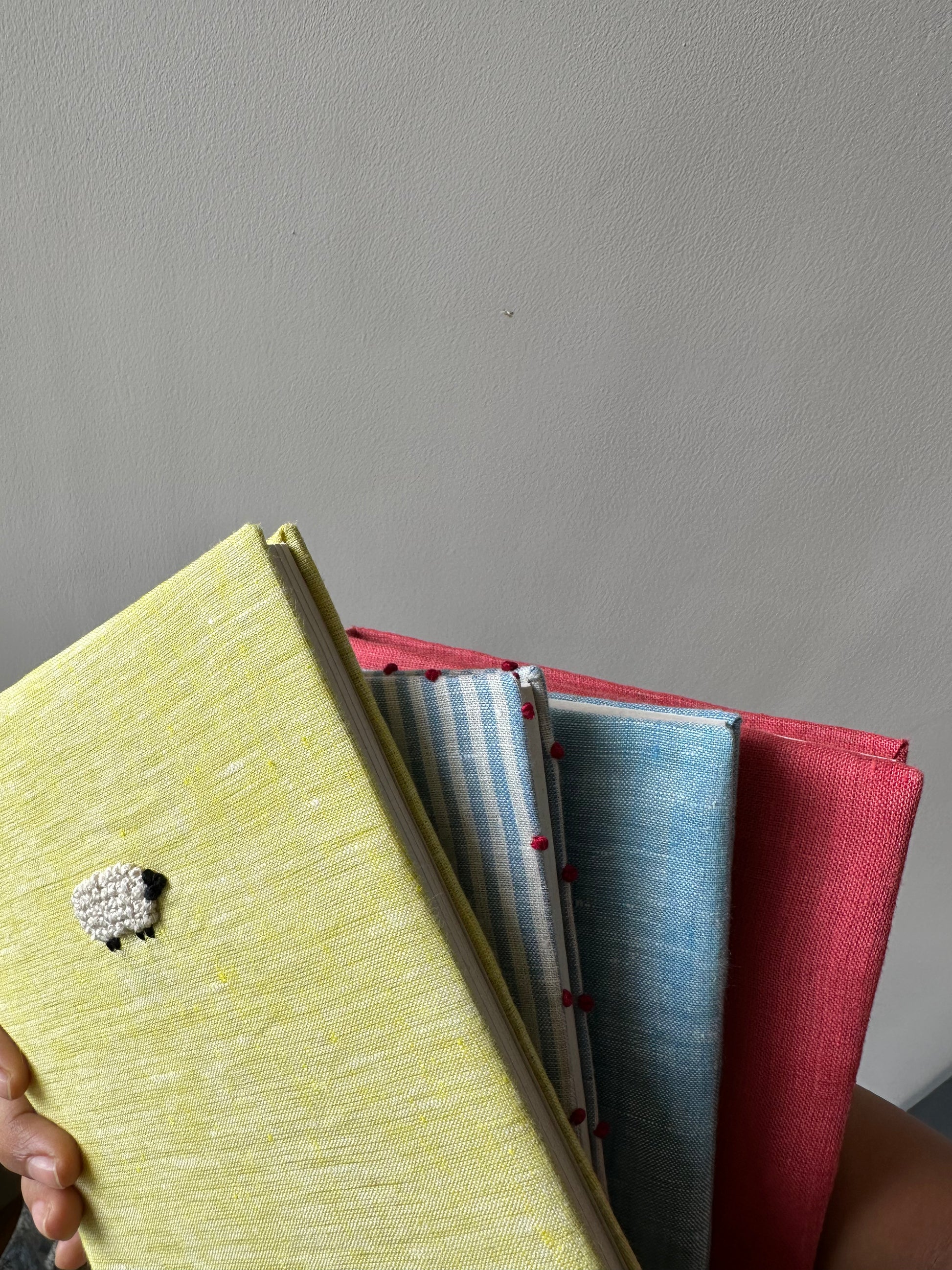 An assortment of hand bound colorful diaries with a diary with an embroidered yellow sheep cover on top