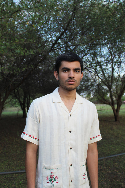 A young man in an off-white cotton shirt with emmbroidered pockets standing in the middle of grove