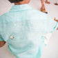 Back details of a young 7-8 year old boy in a blue linen half sleeved shirt with small sheep embroidered throughout is sitting against a white background