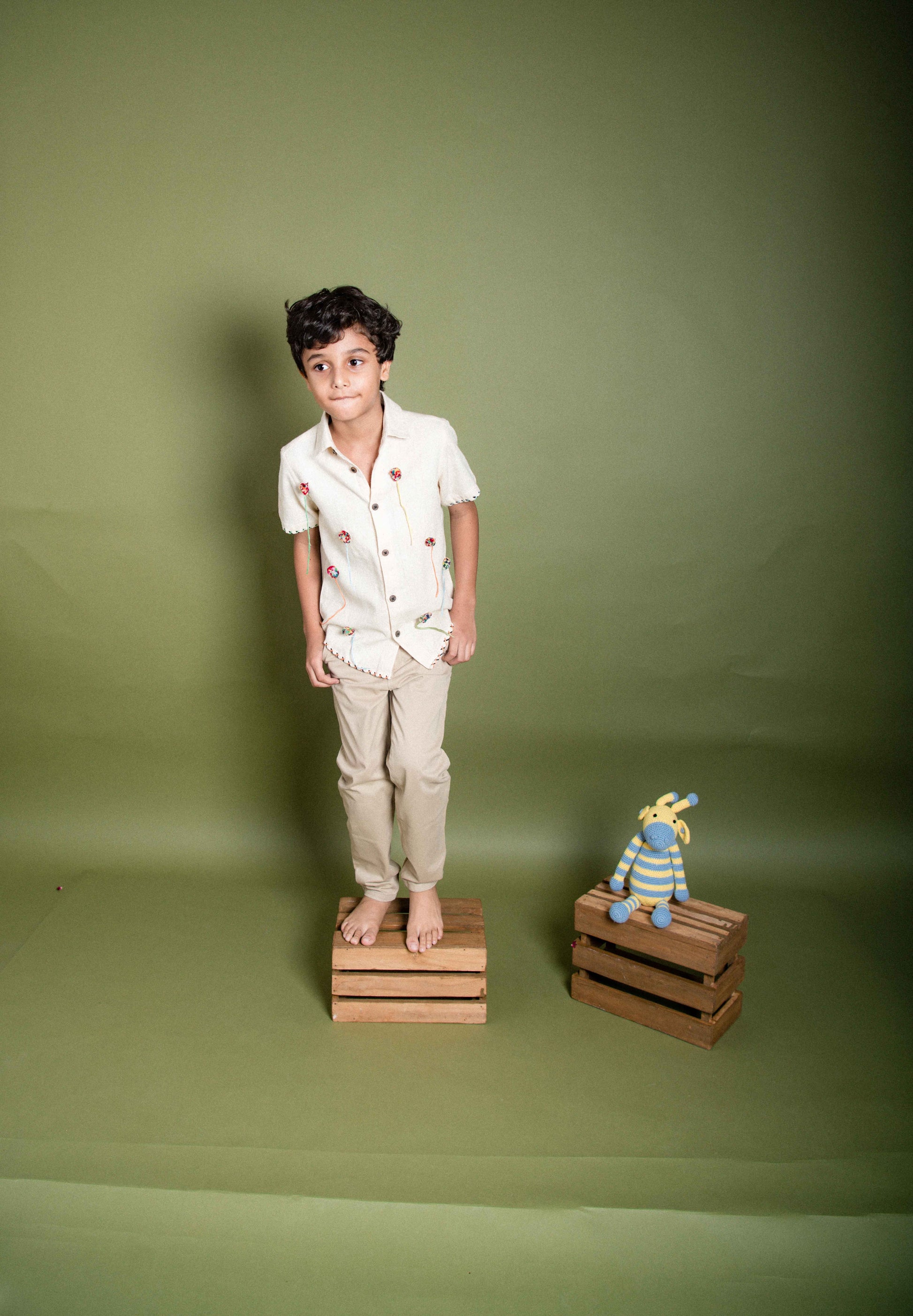 A 6 year old kid in our kala cotton half-sleeved shirt with pom poms embroidered through out standing on a crate