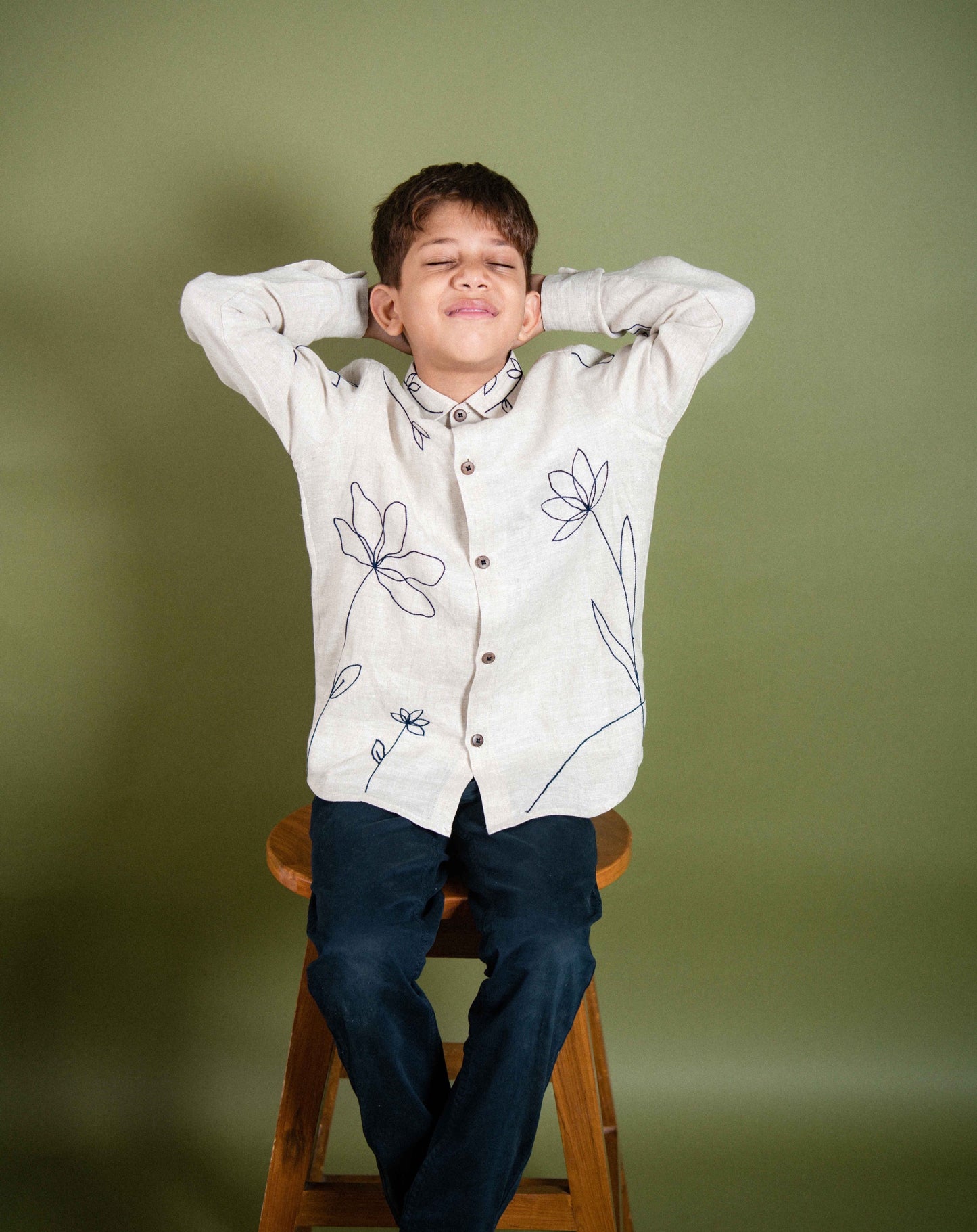 focus on the embroidery detail on a shirt that a 5 year old boy is wearing sitting on a stool