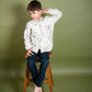 A 5 year old boy in a full sleeved floral embroidered shirt sitting on a stool