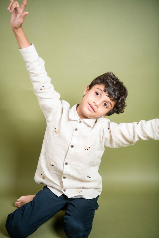 A young 7-8 year old boy in an off-white linen full sleeved shirt with small sheep embroidered throughout 