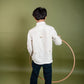 A young 7-8 year old boy in an off-white linen full sleeved shirt with small sheep embroidered throughout. He is playing with a hulahoop and the details of the back are highlighted