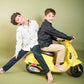 Two boys in beige and black linen shirt playing on a small yellow scooter