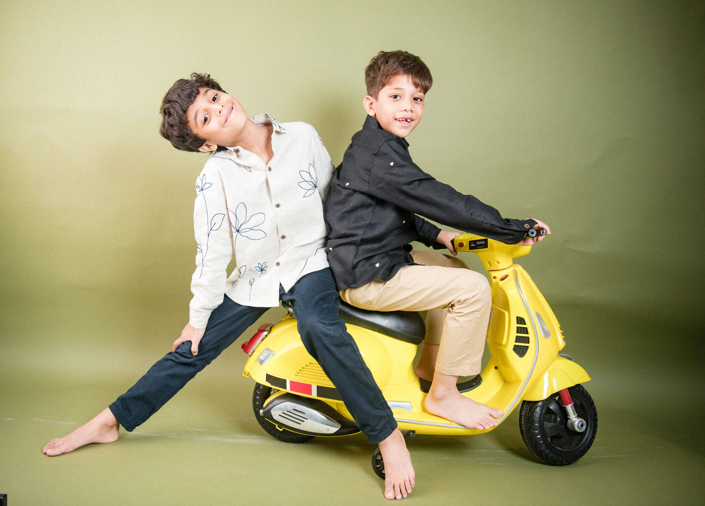 Two boys in beige and black linen shirt playing on a small yellow scooter