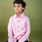 A young 7-8 year old boy in a pink Long sleeved linen shirt is sitting on a crate