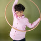 A young 7-8 year old boy in a pink Long sleeved linen shirt is playing with a hula=hoop