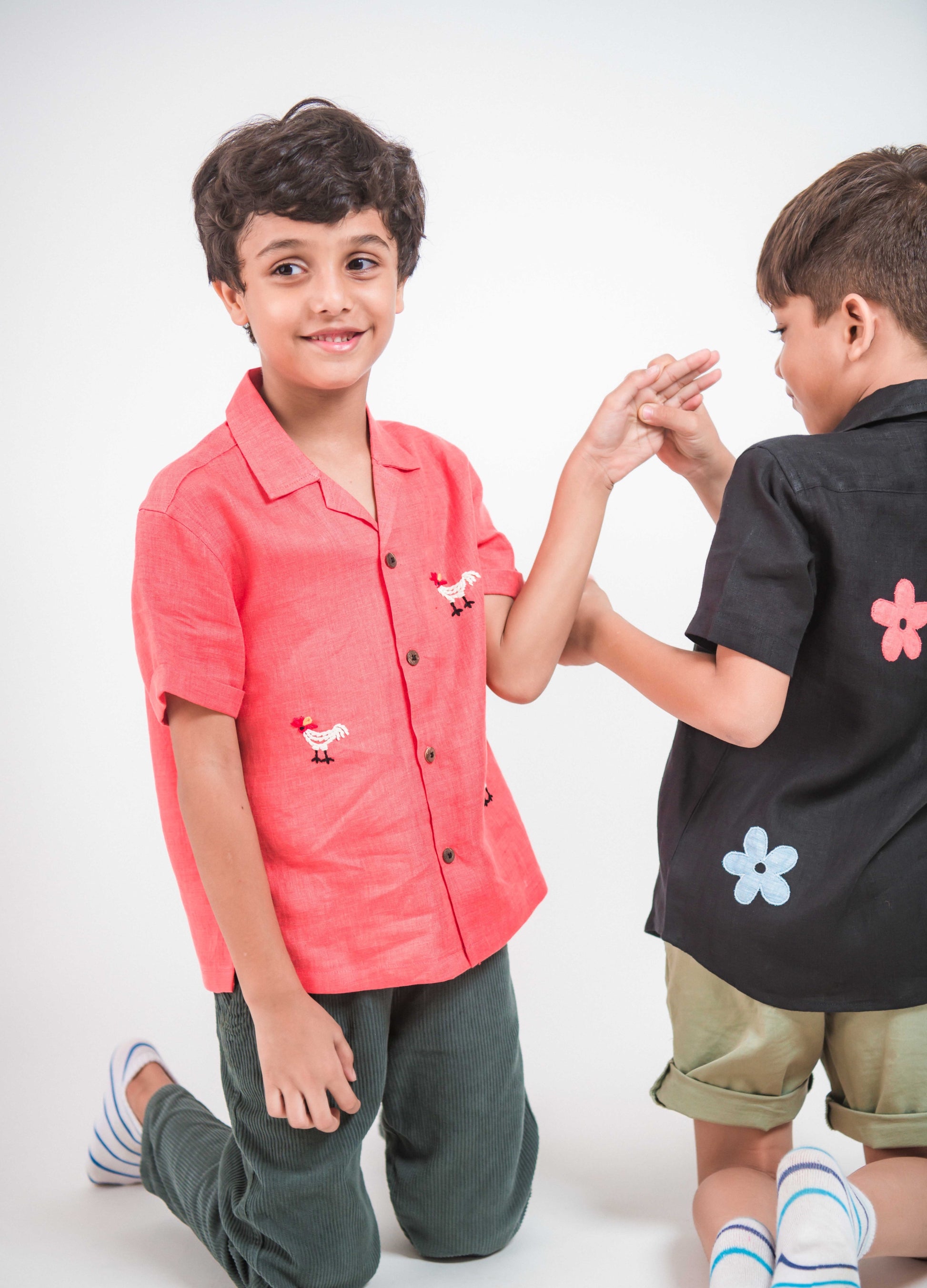 Two young boys in red and black linen shirt with roosters and flowers embroidered respectively