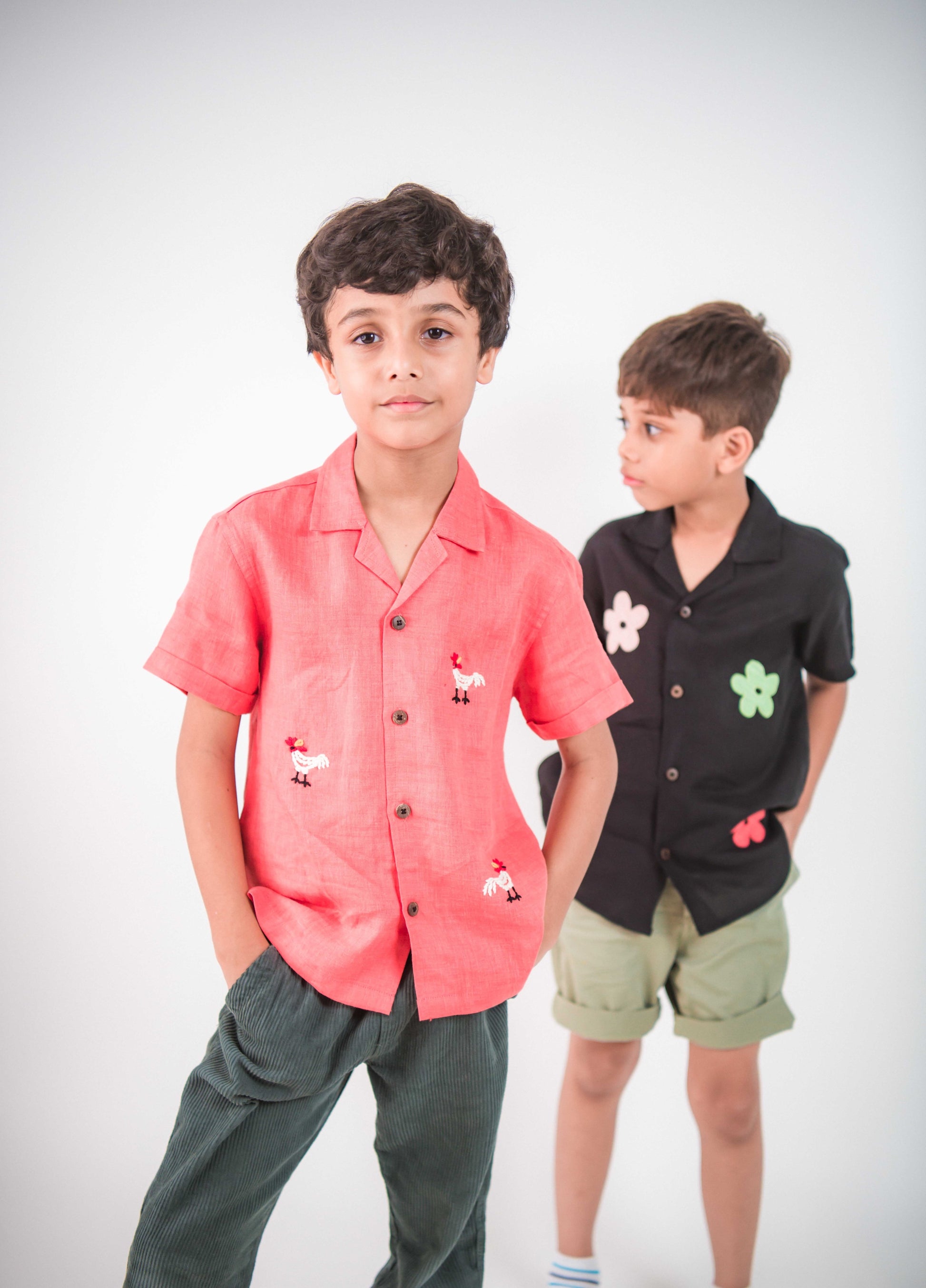 Two young boys in red and black linen shirt with roosters and flowers embroidered respectively