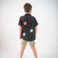 Back of a young 5-6 year old boy in a floral black linen shirt standing against a white background