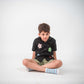 a young 5-6 year old boy in a floral black linen shirt sitting against a white background