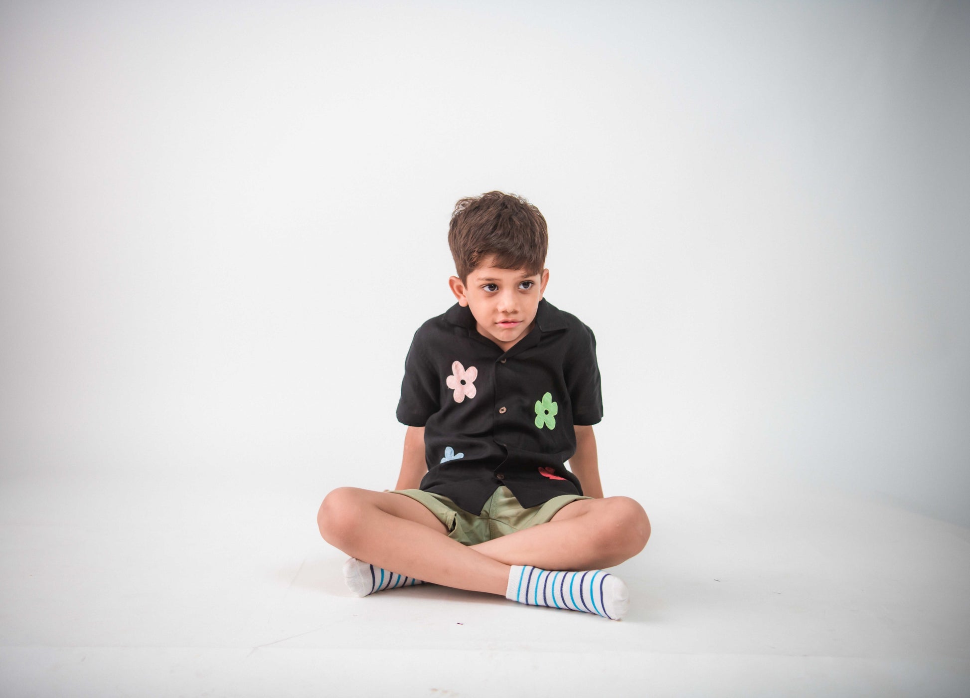 a young 5-6 year old boy in a floral black linen shirt sitting against a white background