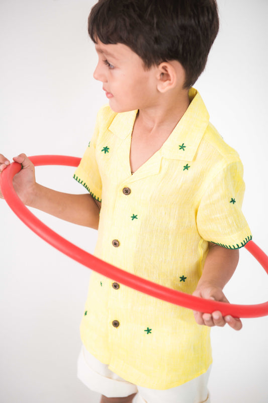 Side view of a small 4-year boy in a yellow linen shirt with small green embroidered flowers is playing with a red hula hoop