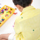 a small 4-year boy in a yellow linen shirt with small green embroidered flowers is sitting and playing with legos