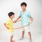 two young boys in yellow and blue half sleeved linen shirts playing with a hulahoop