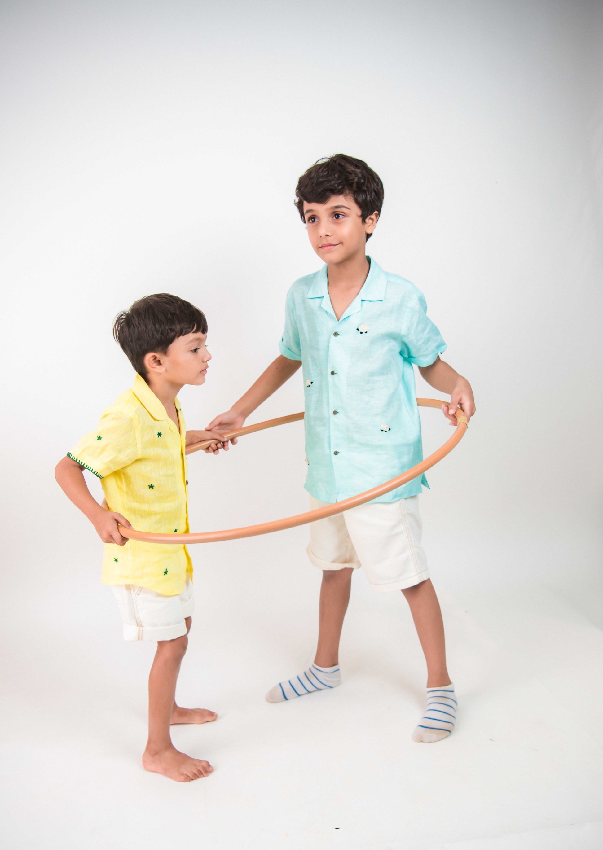 two young boys in yellow and blue half sleeved linen shirts playing with a hulahoop