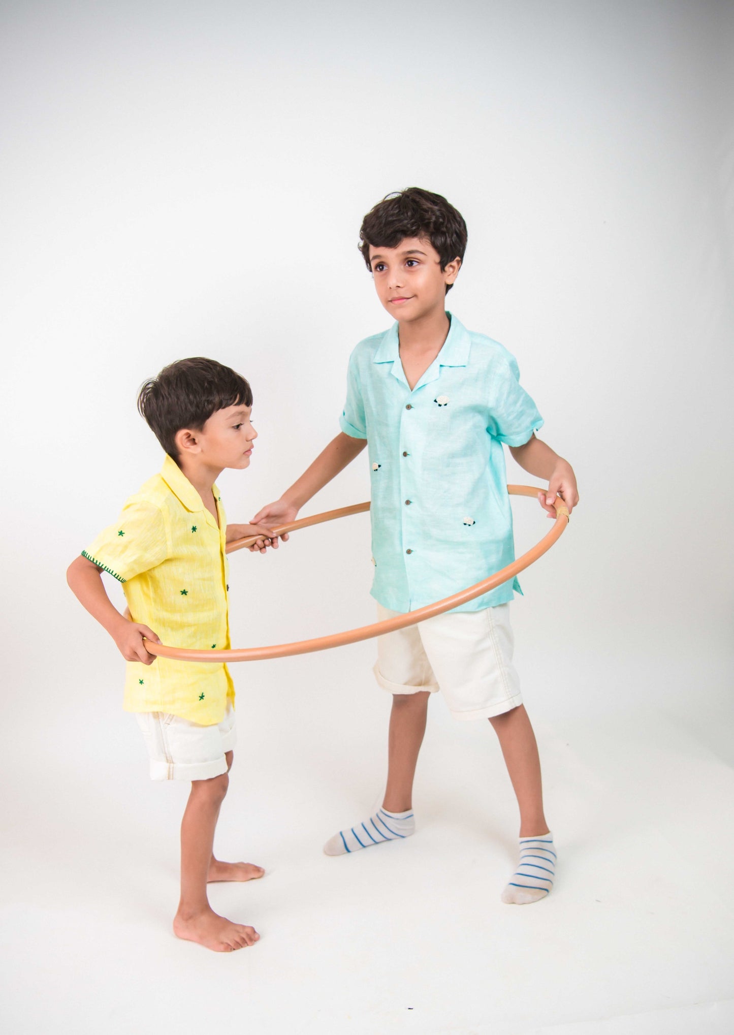 Two boys in yellow and blue linen embroidered shirts are playing with hula-hoops