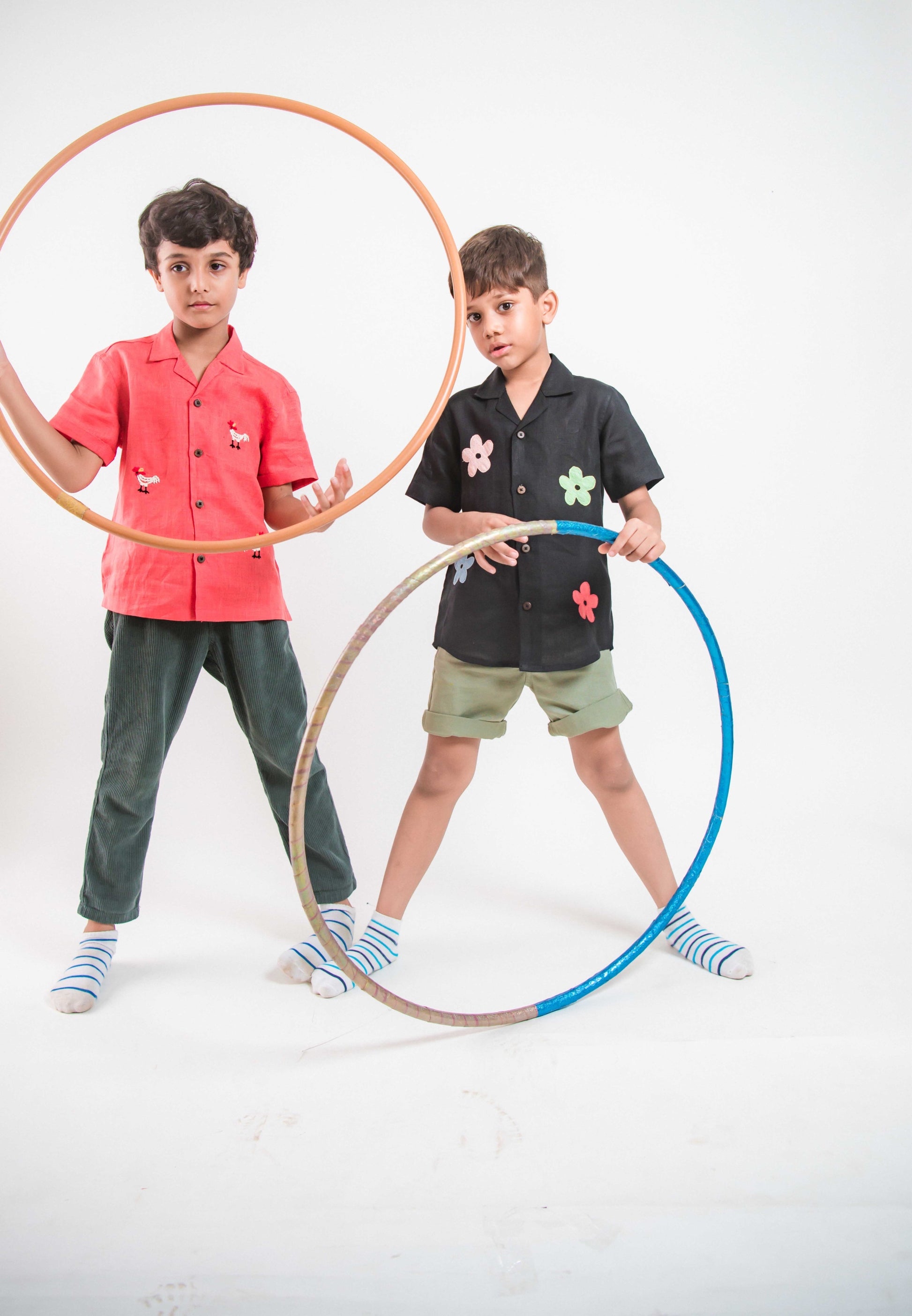 two boys in red and black linen shirts respectively playing with hulahoops