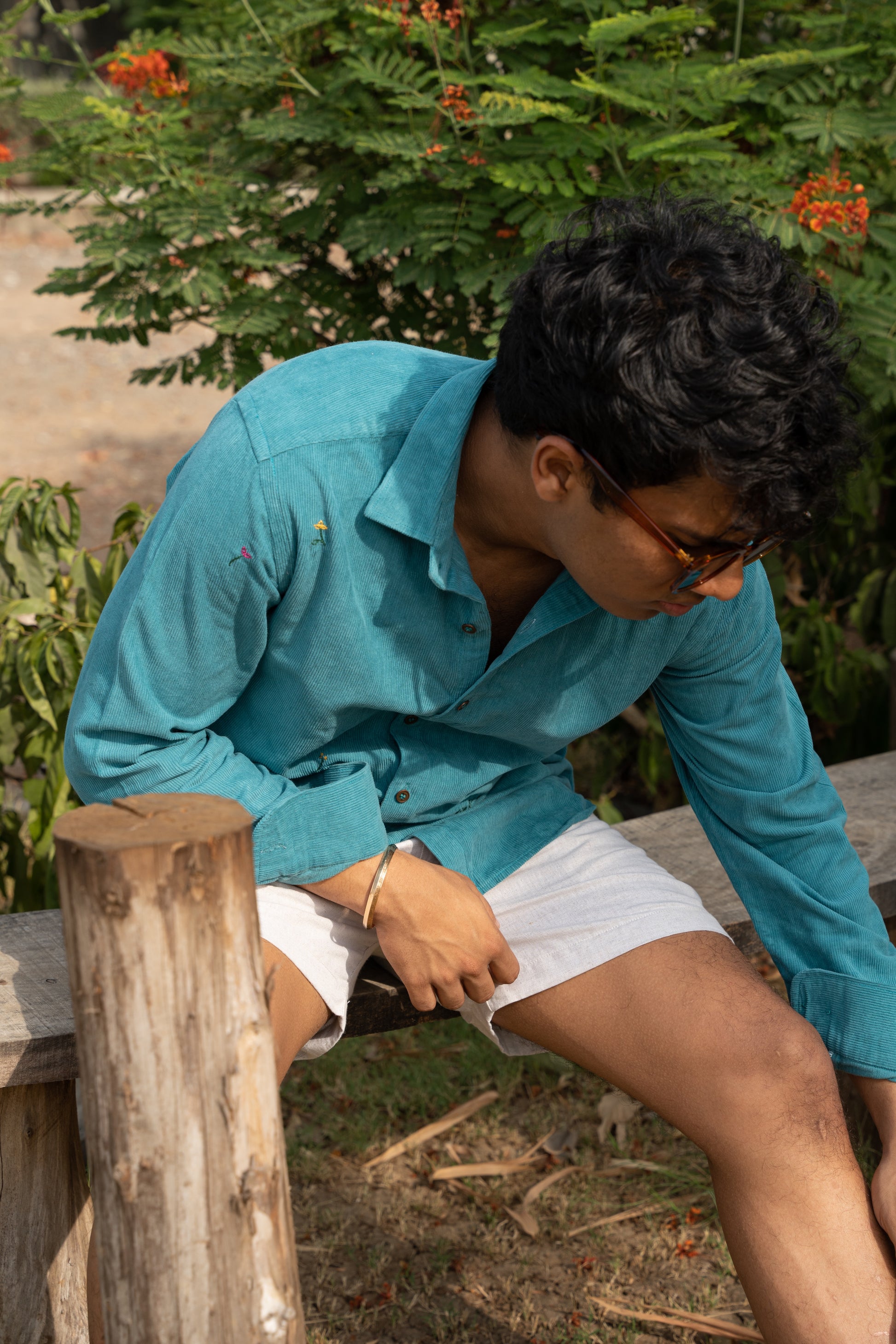 Pranav in teal cotton corduroy teal overshirt with small hand-embroidered flowers is standing in front of trees