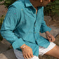 Pranav in teal cotton corduroy teal overshirt with small hand-embroidered flowers is standing in front of trees 