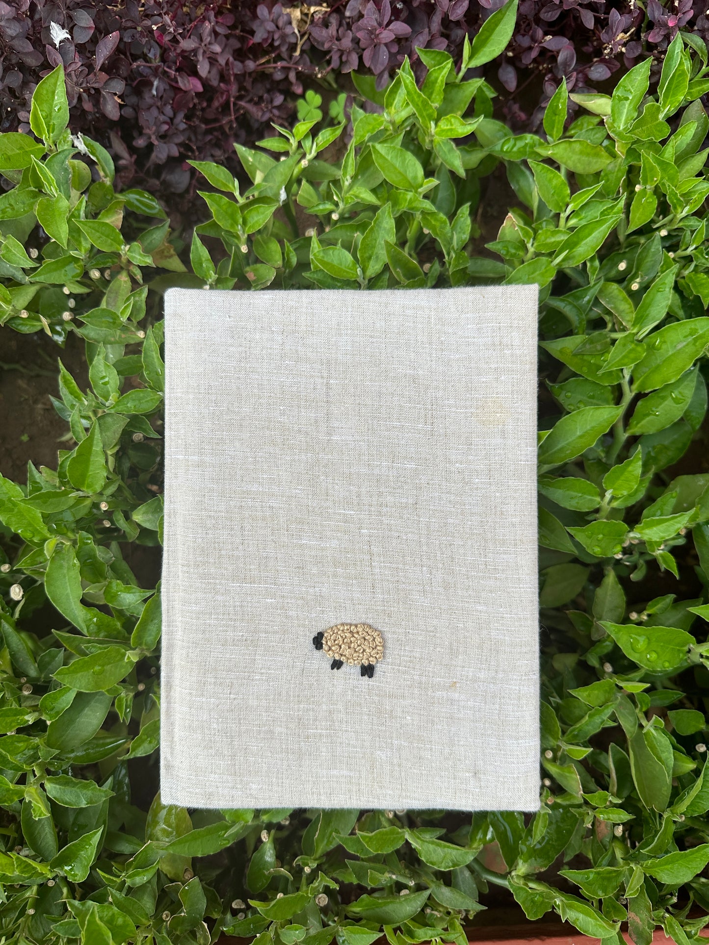 An offwhite diary made with offwhite linen scraps with a light brown sheep embroidered on the cover