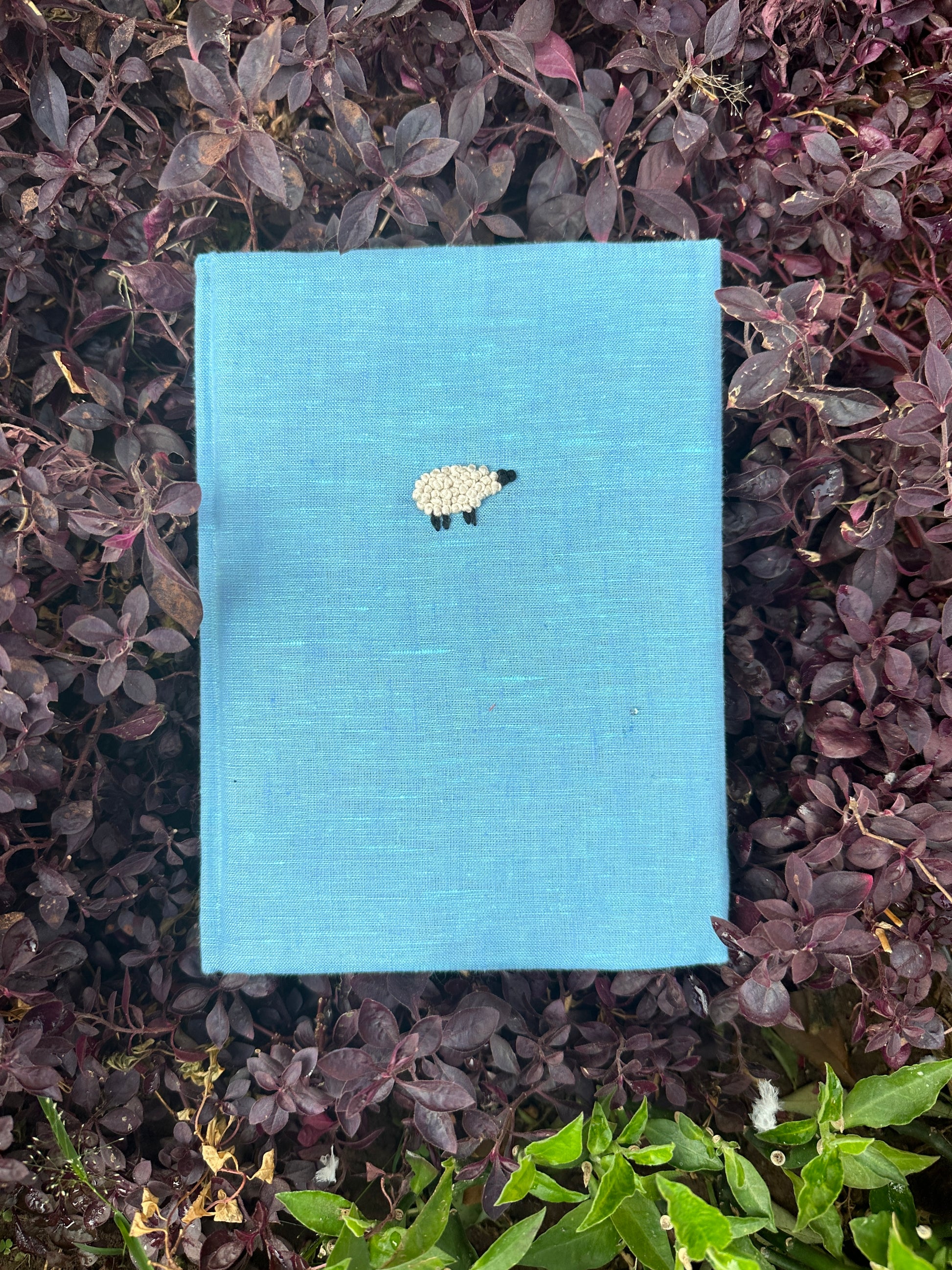 A blue diary made with light blue linen scraps with a white sheep embroidered on the cover