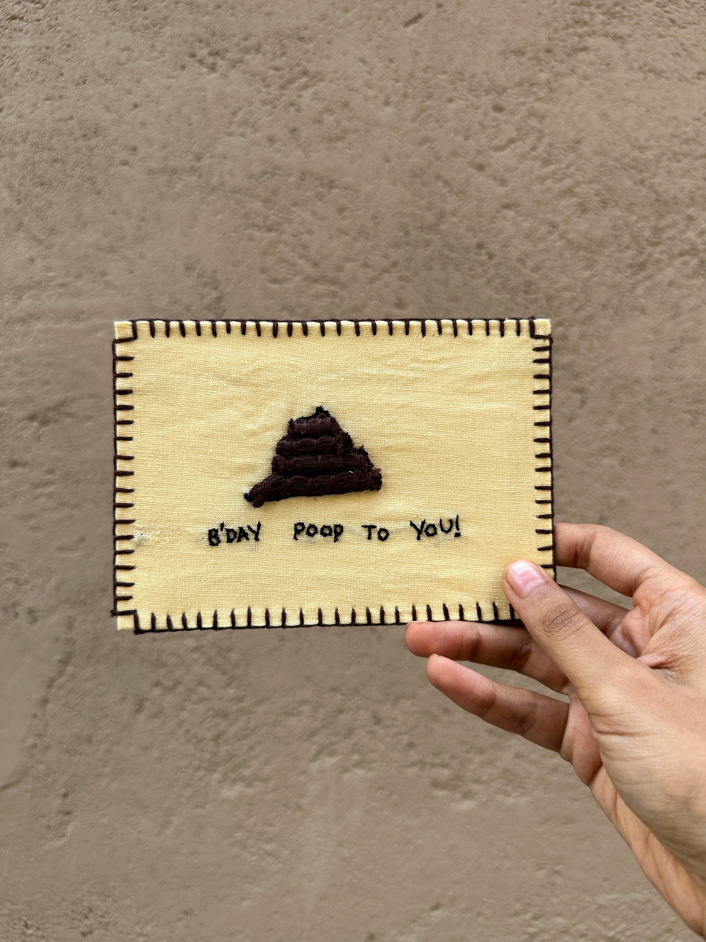 Hand-embroidered postcard featuring a playful poop emoji with the text 'B'day poop to you,' crafted from sustainable linen