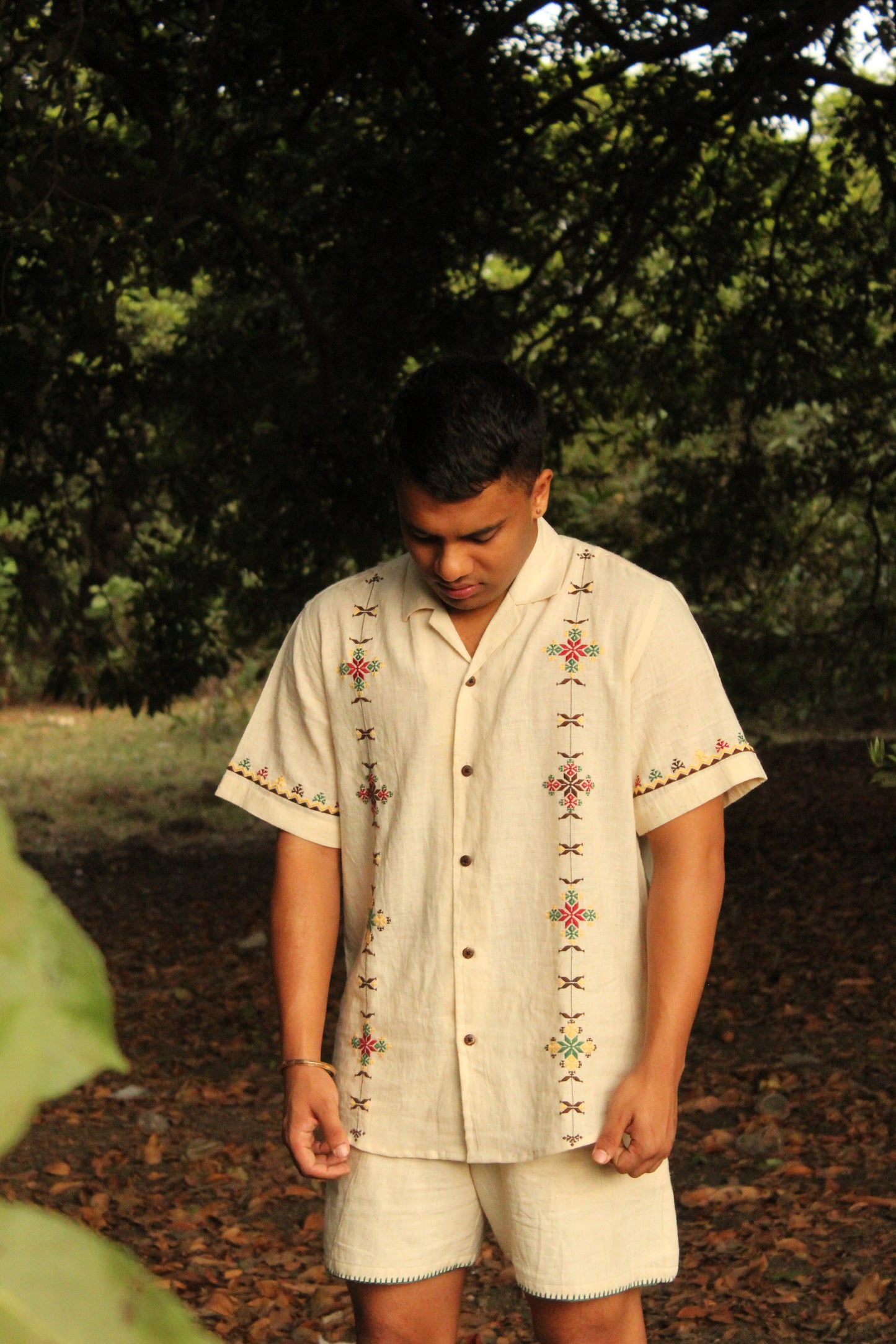 Pranav in an off-white kala cotton hand-embroidered shirt is standing in a forest 