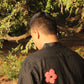 Back of a young man in a black linen shirt with colorful flowers against a backdrop of trees