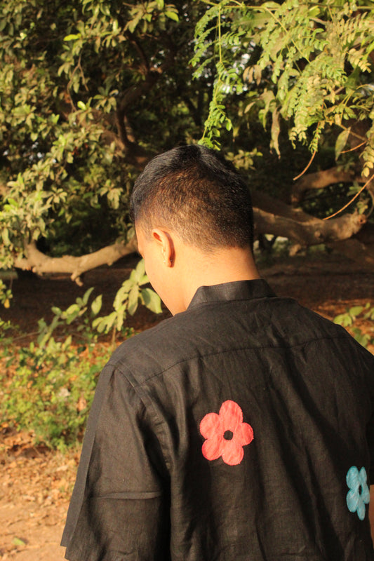 Back of a young man in a black linen shirt with colorful flowers against a backdrop of trees