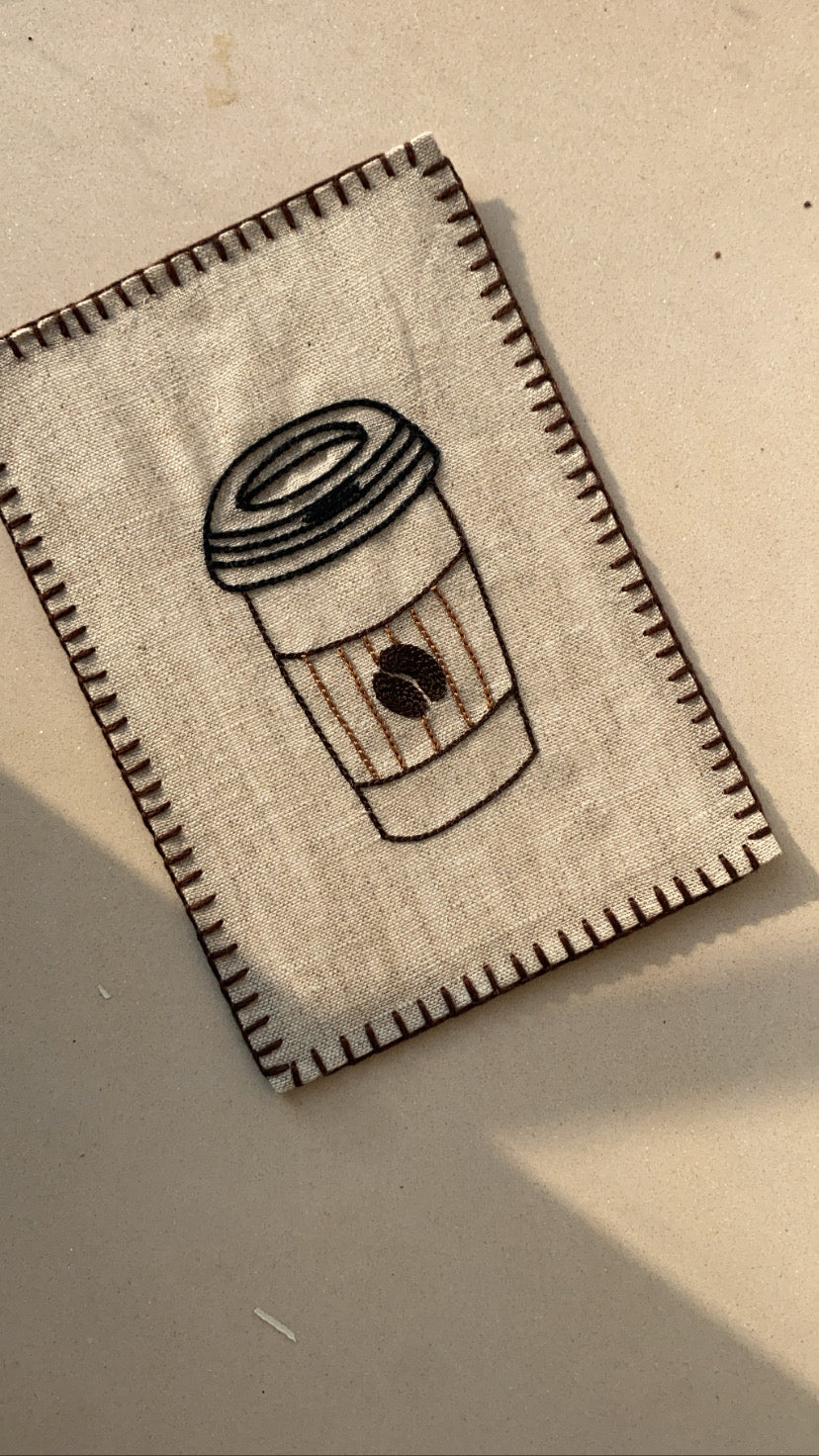 Close-up view of intricate hand embroidery showing a coffee cup on the postcard, highlighting the artistry