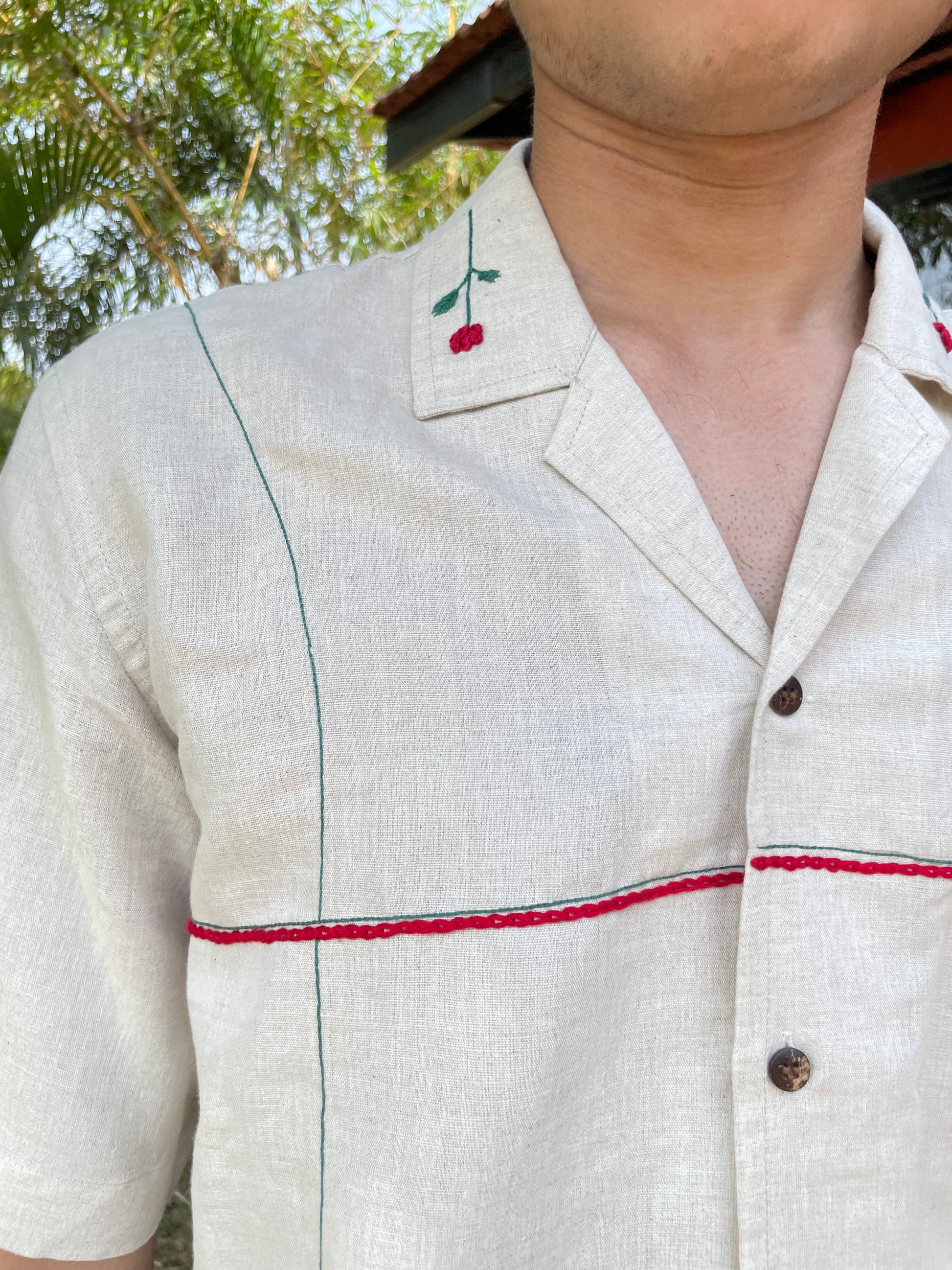 Details of a beige linen shirt with hand-embroidered rose on the collar and horizontal and vertical lines passing in green and red colors