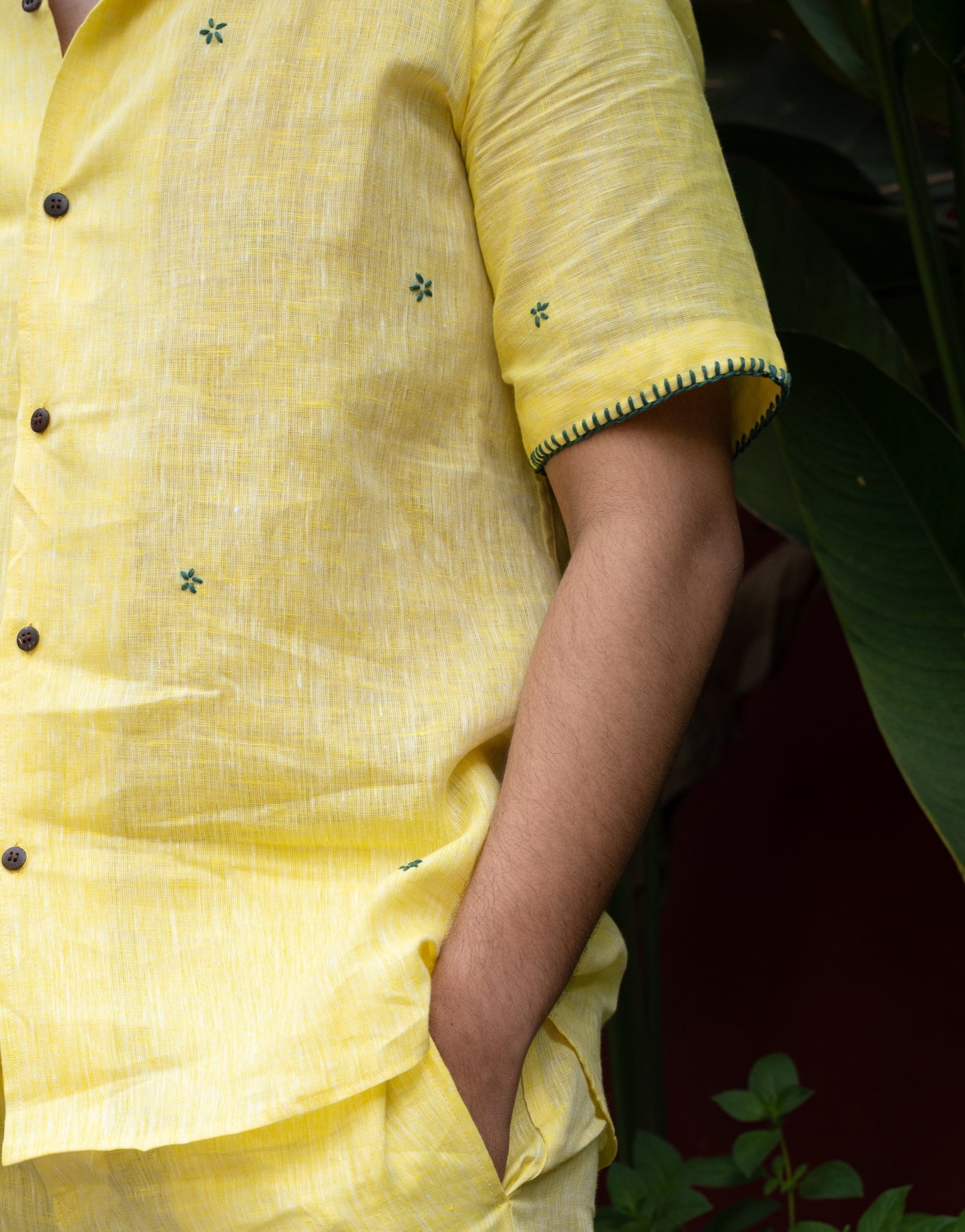 Details of a yellow linen shirt with small green flowers embroidered throughout and border details on the sleeve