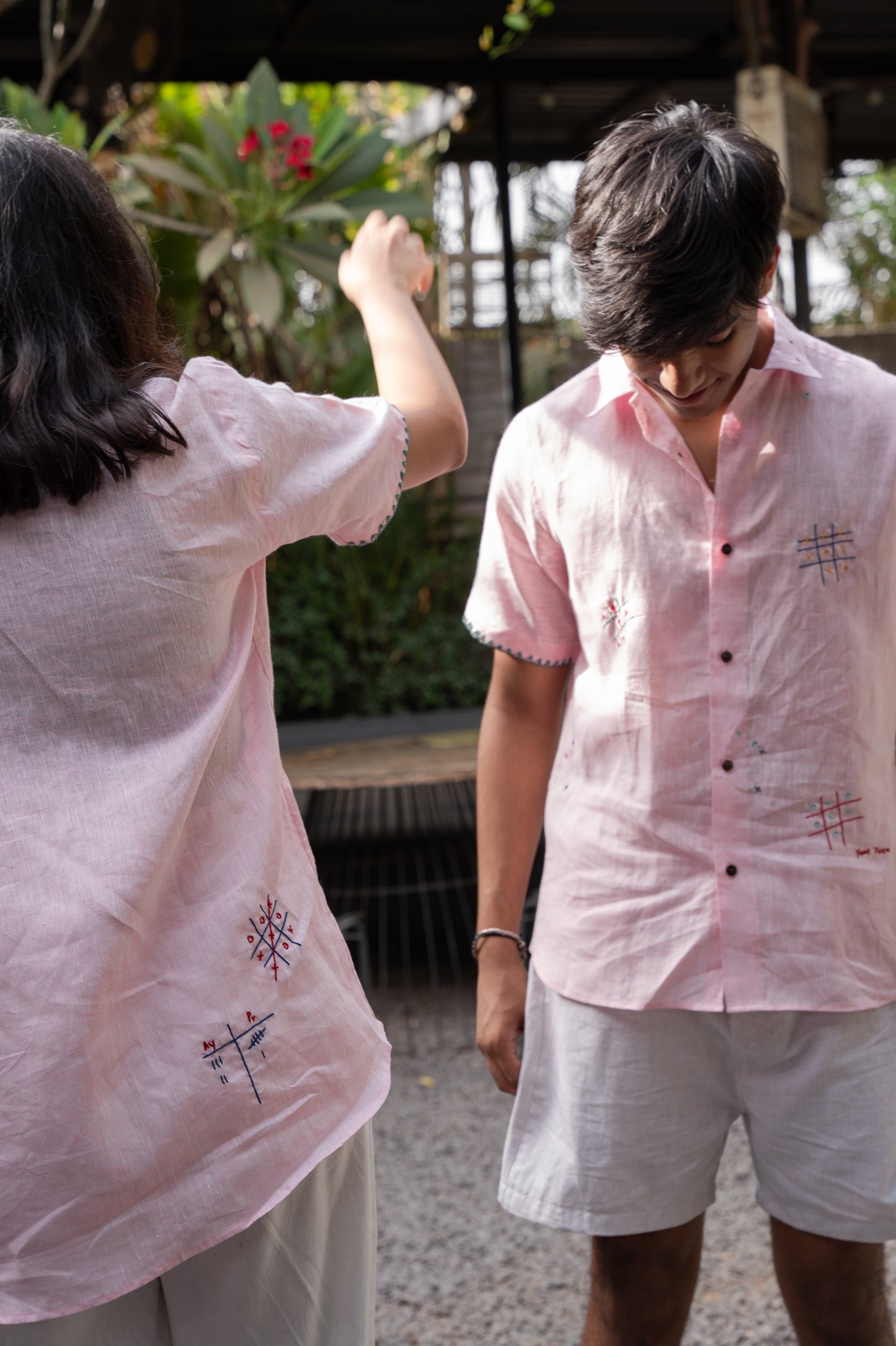 A girl and a boy in pink linen shirts with hand-embroidered tic tac toes