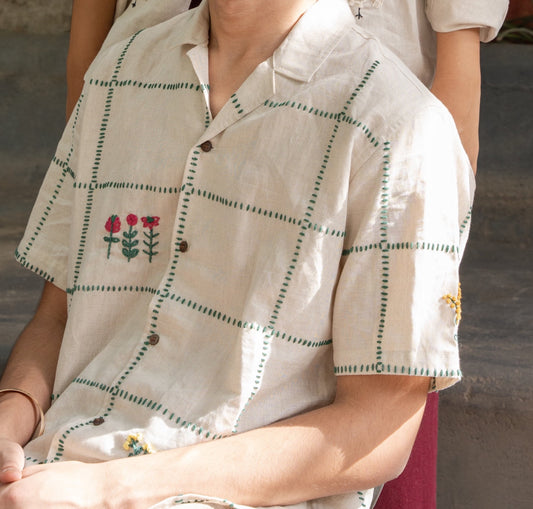 Front details of a beige linen shirt featuring a hand-embroidered grid with flowers and small animals placed randomly