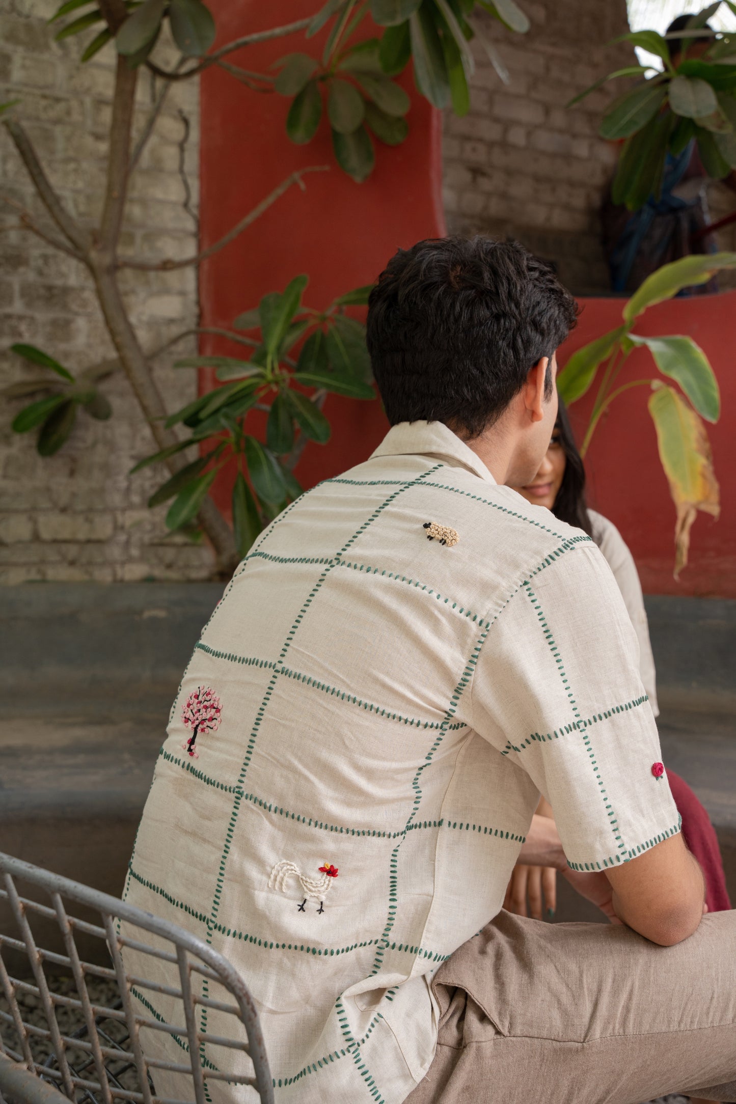 Back details of a beige linen shirt featuring a hand-embroidered grid with flowers and small animals placed randomly