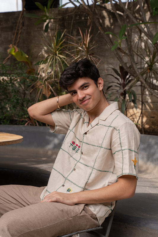 Soham in a beige linen shirt featuring a hand-embroidered grid with flowers and small animals placed randomly